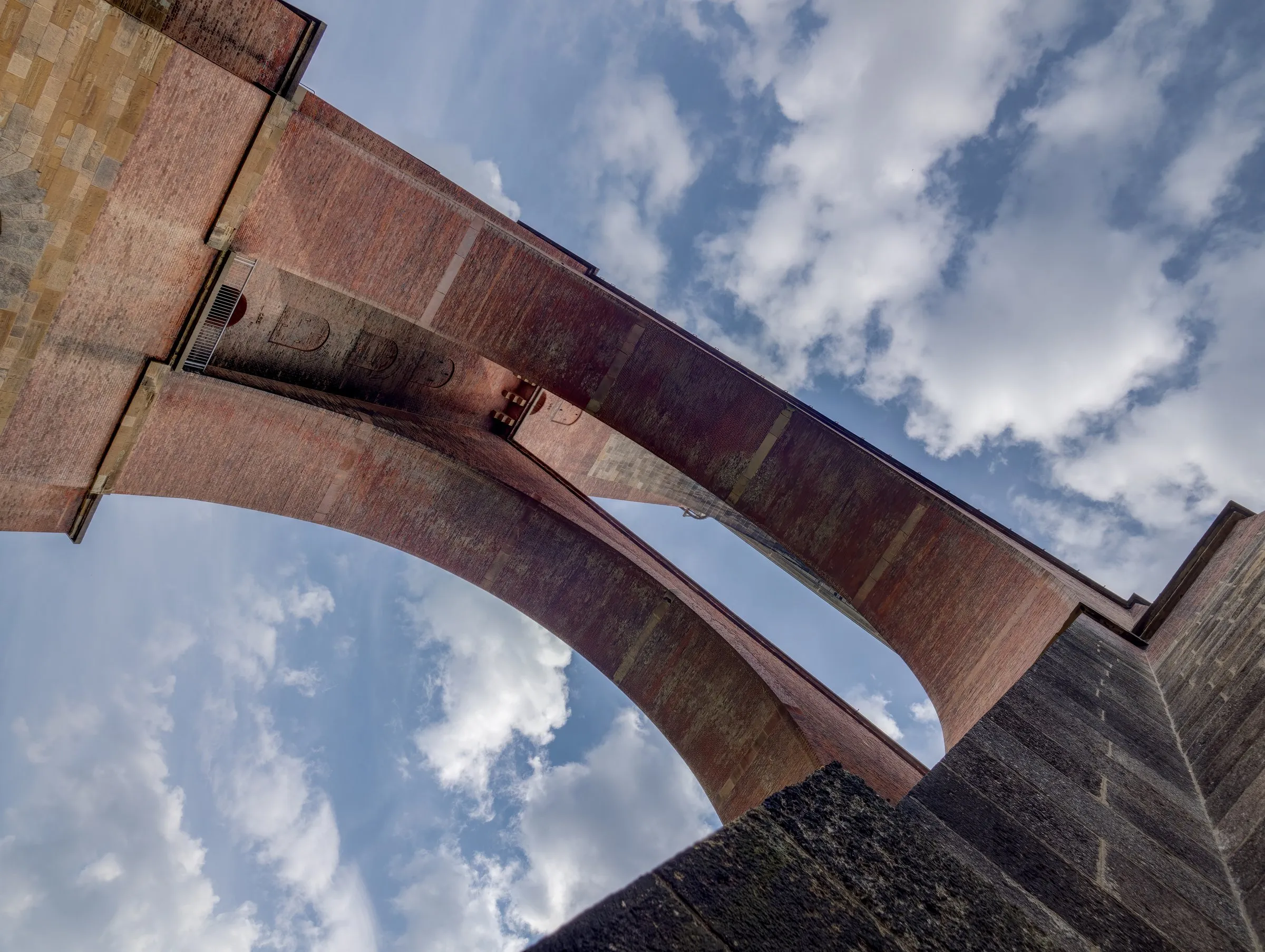Blick von unten auf die Ziegelbögen der Göltzschtalbrücke, dahinter blauer Himmel mit Schönwetterwolken