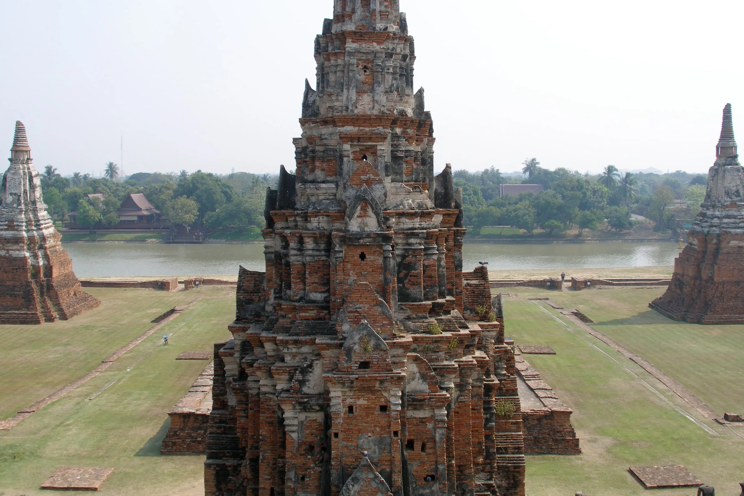 Backsteinturm des Tempels Wat Chaiwatthanaram in Ayutthaya, dahinter der Fluss und flaches grünes Land