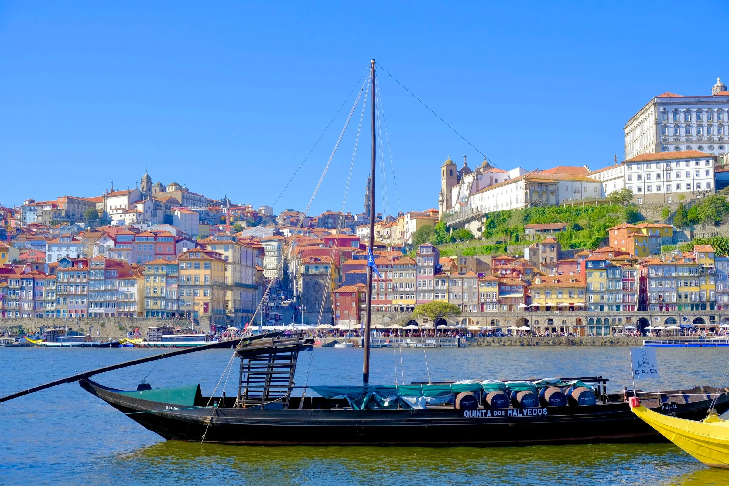 Traditionelles Rabelo-Boot auf dem Douro in Porto, dahinter die bunten Häuser der Altstadt am Hang unter blauem Himmel