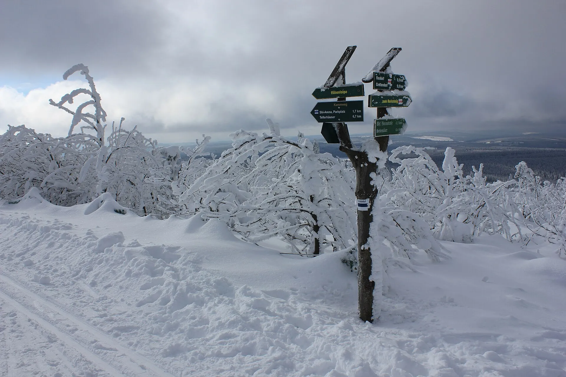Verschneiter Wegweiser zu Kammweg und Höhenloipe zwischen tief verschneiten Bäumen auf dem Fichtelberg