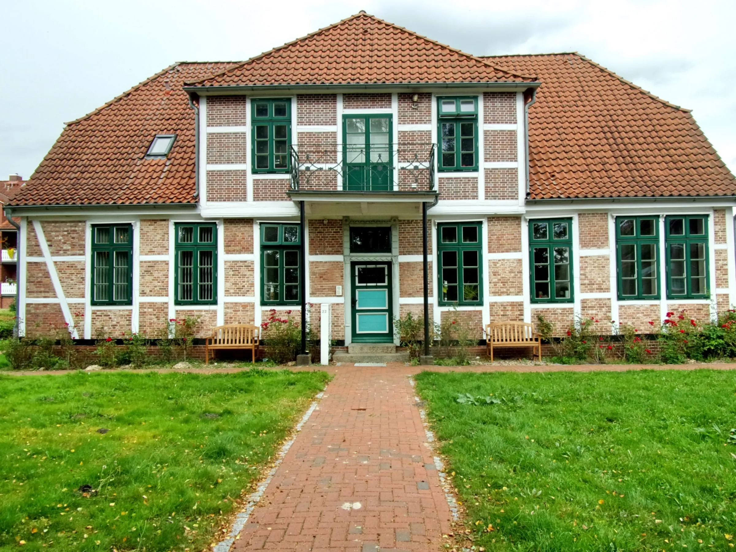 Altländer Fachwerkhaus mit Backsteingefachen, grünen Fensterläden und rotem Ziegeldach hinter einem Rasenstück