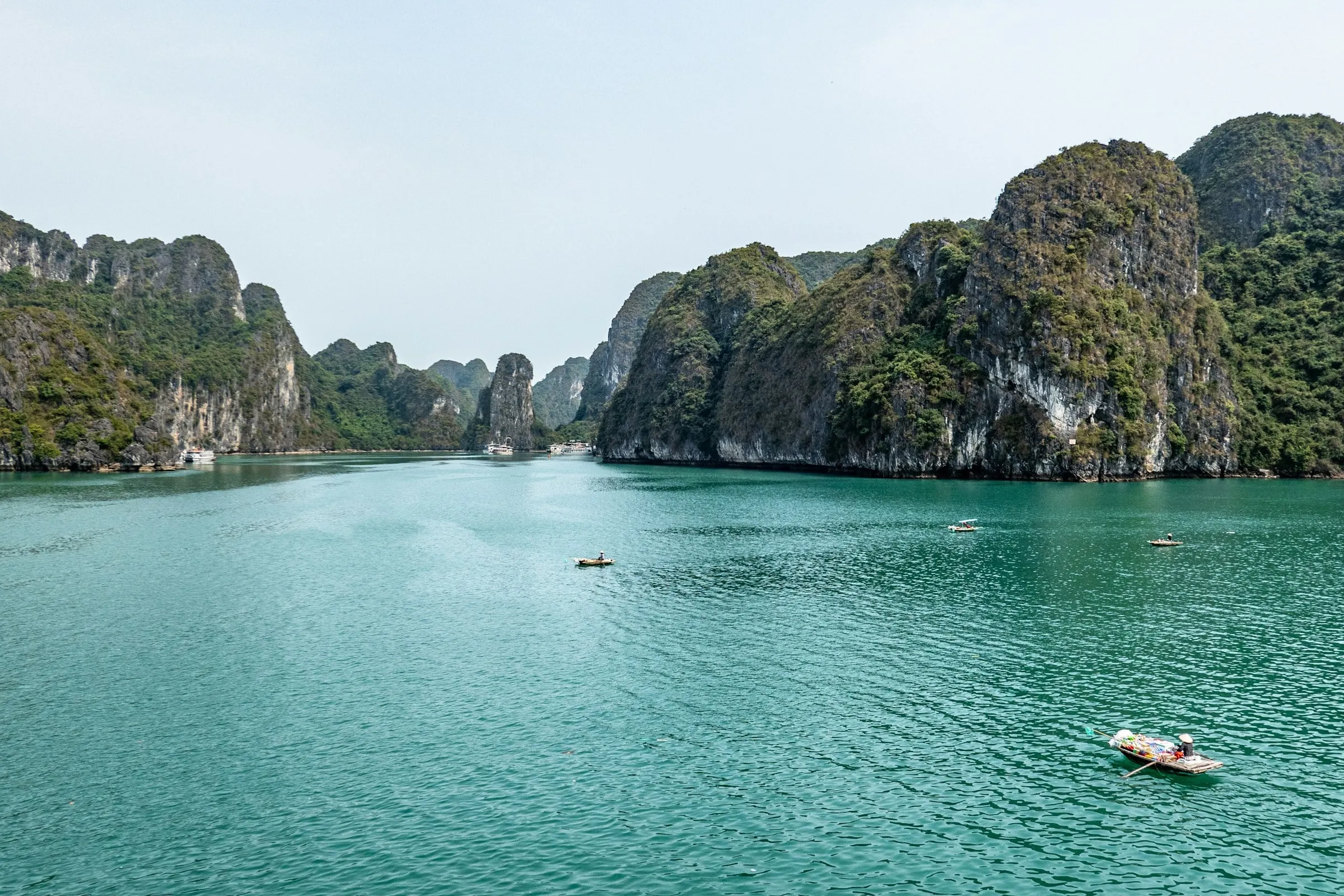 Grüne Kalksteinfelsen ragen aus dem türkisfarbenen Wasser der Ha-Long-Bucht, dazwischen kleine Ruderboote