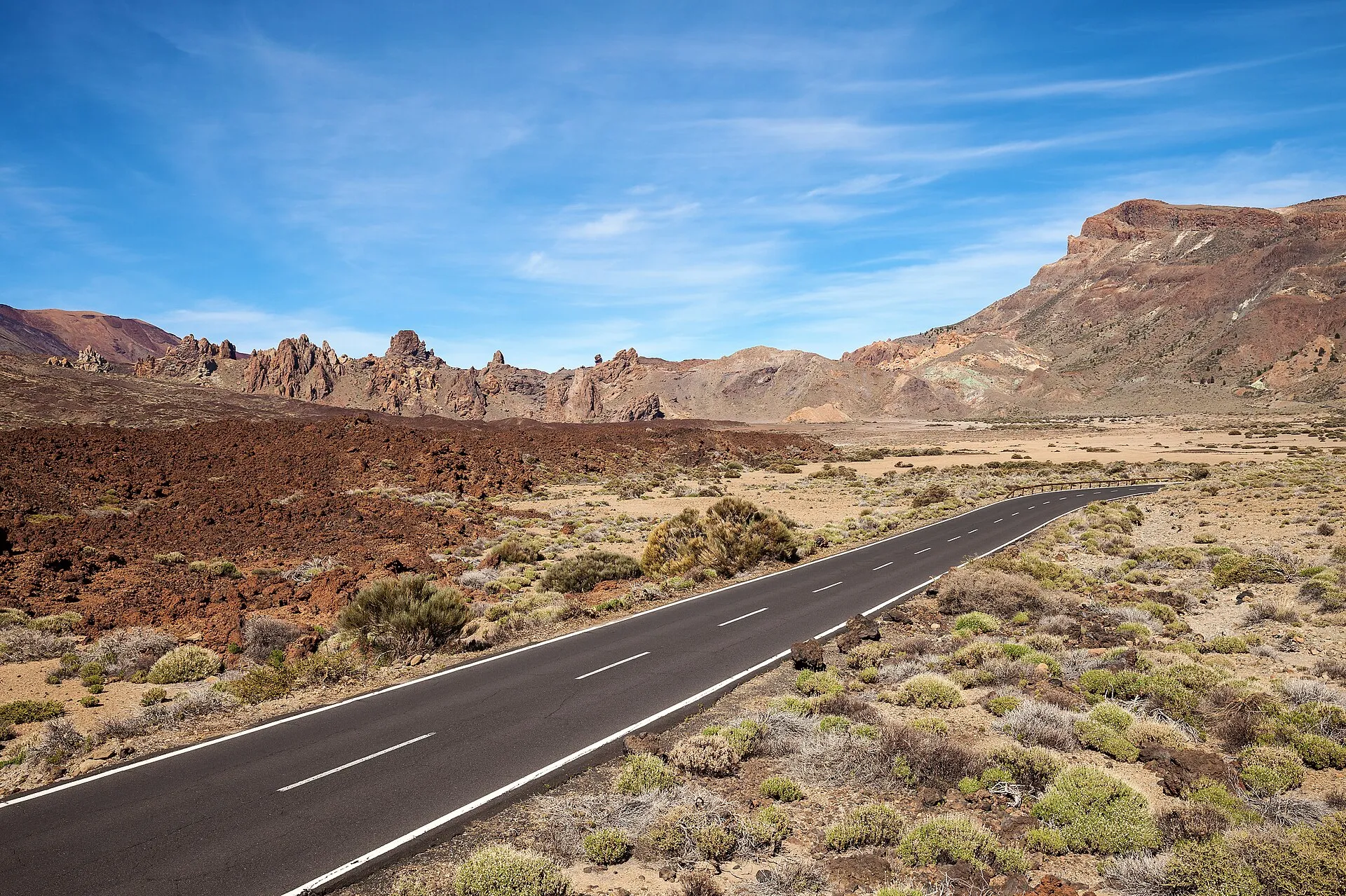 Leere Straße durch die Vulkanlandschaft der Cañadas, links rotbraune Lava und die Felstürme der Roques de García