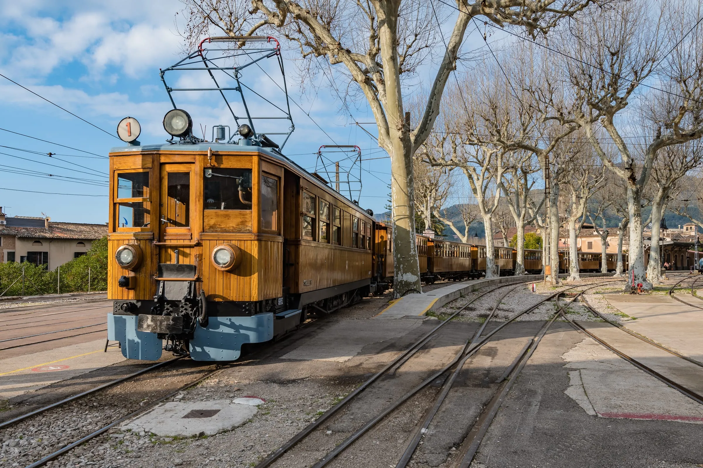 Historischer Holztriebwagen der Bahn nach Sóller mit Oberleitung am Bahnhof, daneben kahle Platanen und Gleise